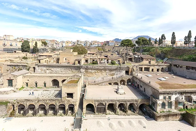 Las excavaciones de Herculano con los arcos de las cocheras de barcas, la ciudad moderna y el Vesubio al fondo